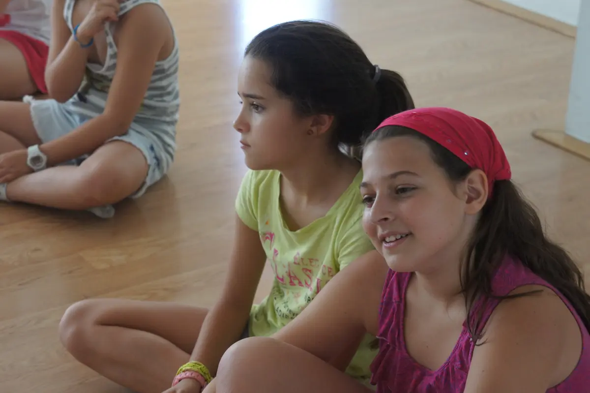 Dos alumnas sentadas en el suelo de la sala, en clase.