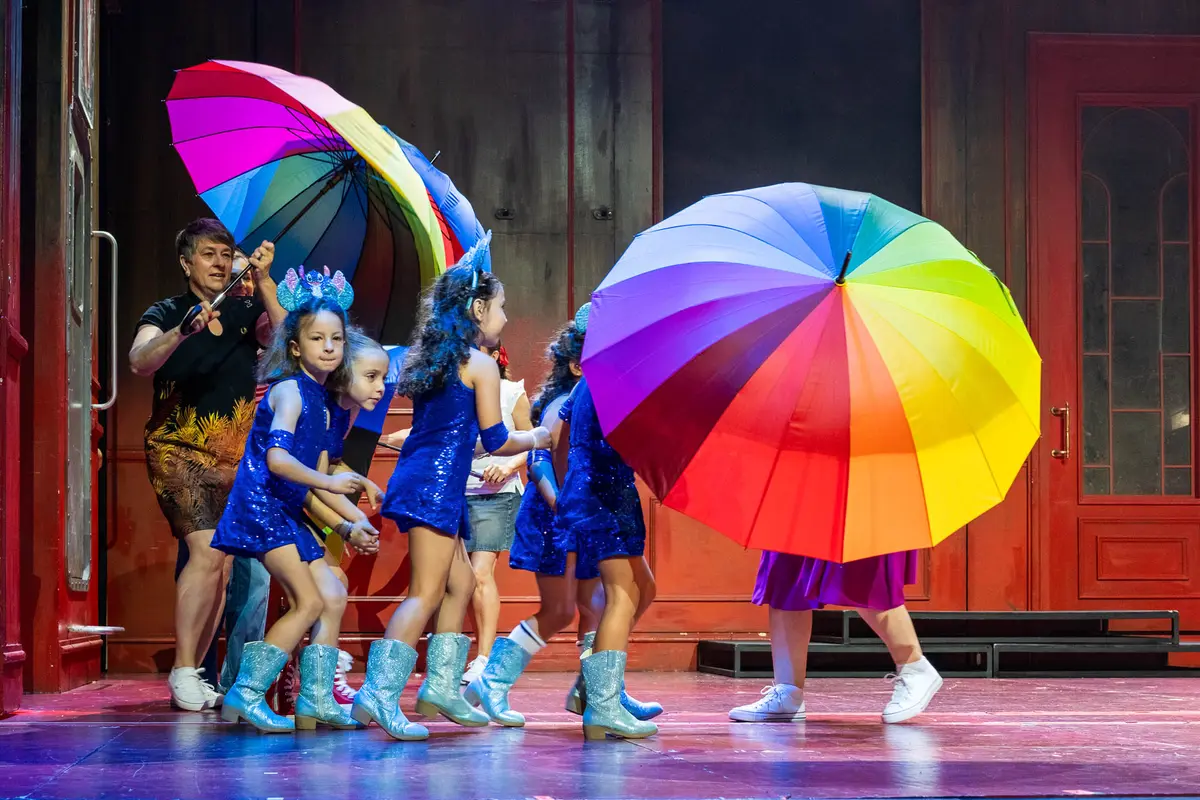 Alumnas pequeñas con paraguas de colores en el escenario.