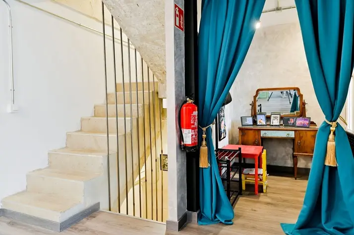 Escalera de hormigón y camerino con cortinas turquesa y tocador antiguo.