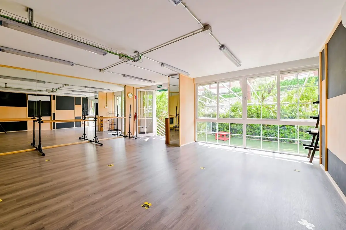 Sala grande con barras de danza, suelo de madera y ventanal al jardín.