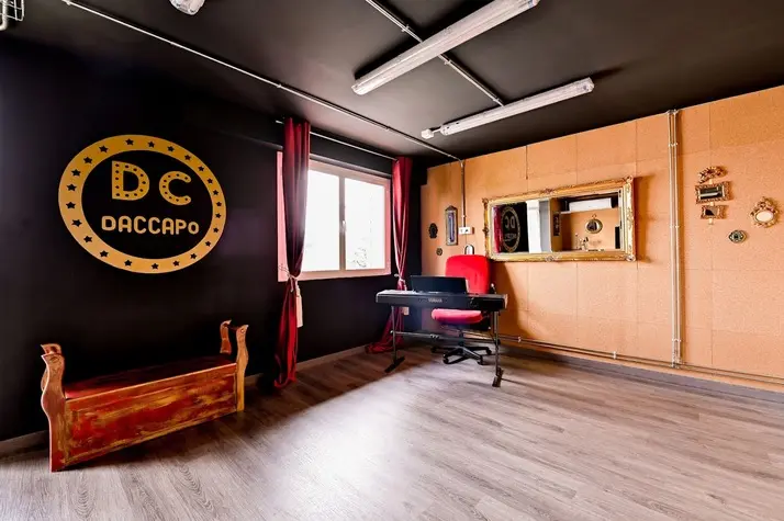 Sala con el sello DC dorado en la pared negra, cortinas rojas y espejo de camerino.