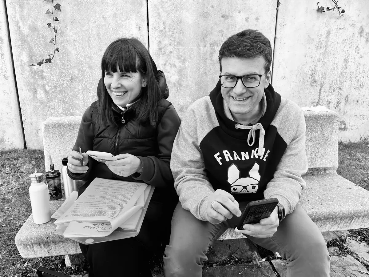 En blanco y negro, una mujer y un hombre sonríen sentados con papeles en la mano.